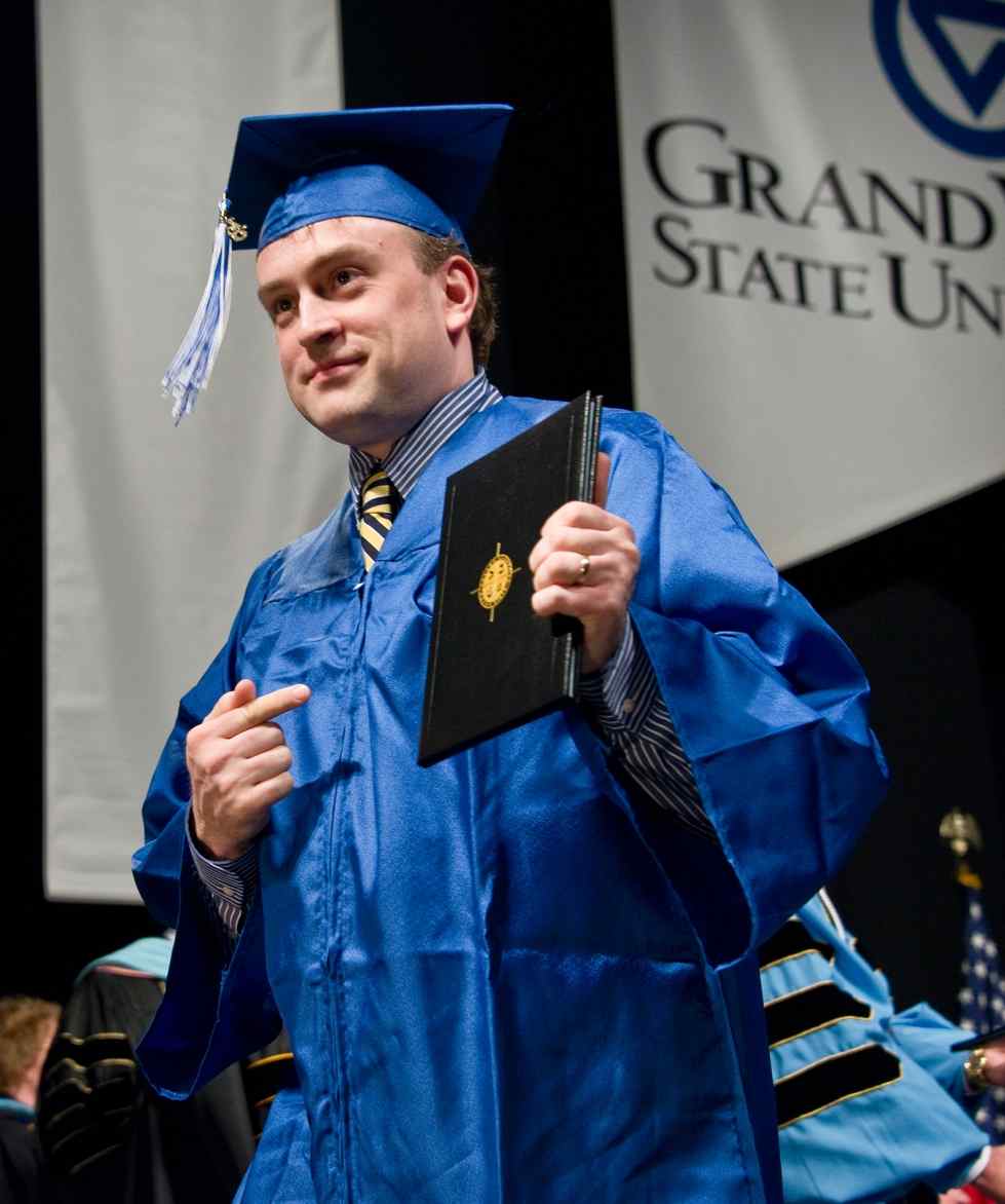 Student in blue graduation cap and gown holding his diploma